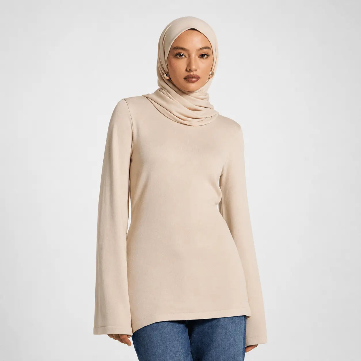 Woman wearing a beige hijab and long-sleeve top on a white background