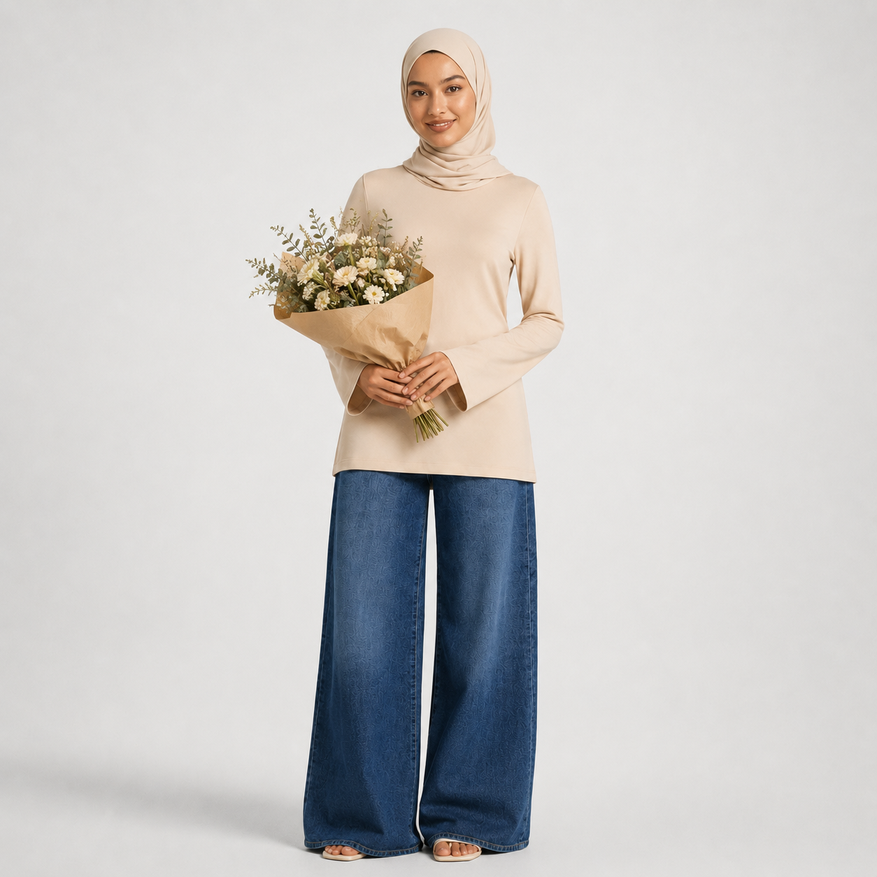 Woman holding a bouquet of flowers wearing a beige top and blue jeans on a white background