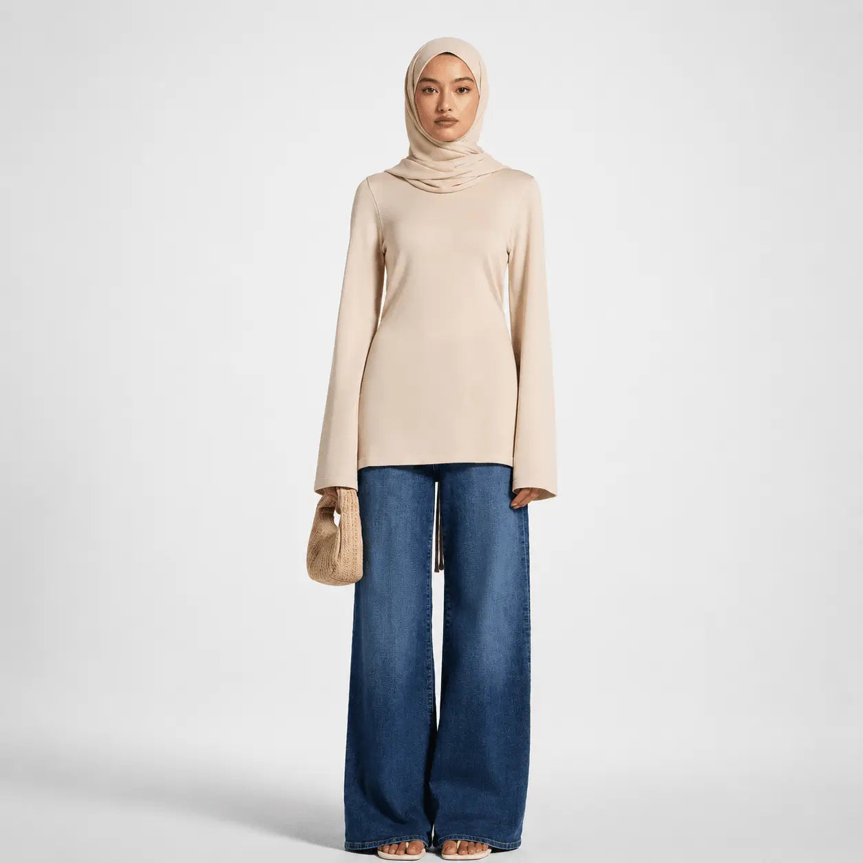 Woman wearing a beige hijab, beige top, and blue jeans on a white background
