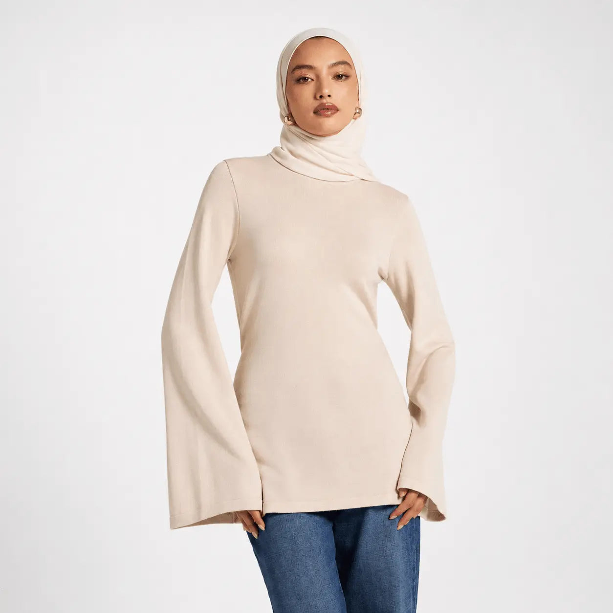 Woman wearing a beige turtleneck sweater and blue jeans on a white background