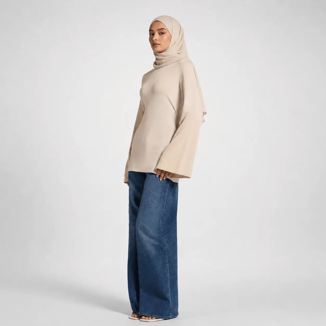 Woman wearing a beige top and blue jeans on a white background