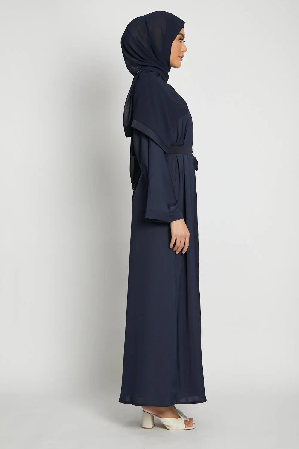 Woman wearing a navy blue abaya and hijab on a white background