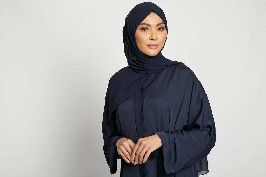 Woman wearing a navy blue hijab and abaya against a white background