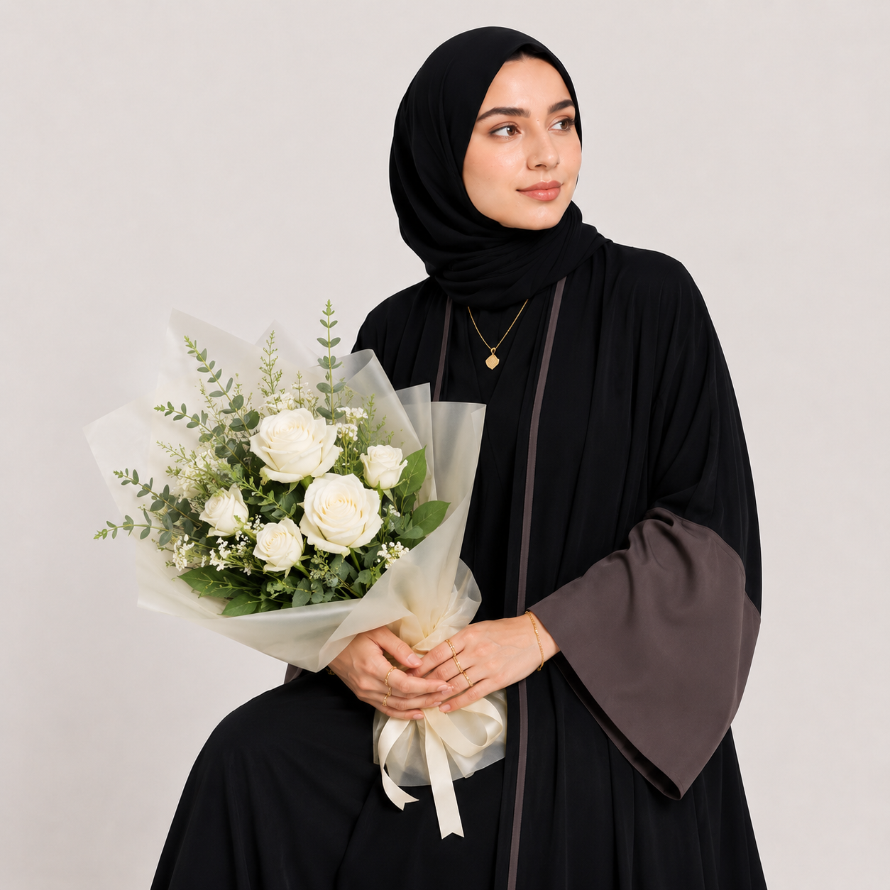 Woman in black hijab holding a bouquet of white flowers against a plain background
