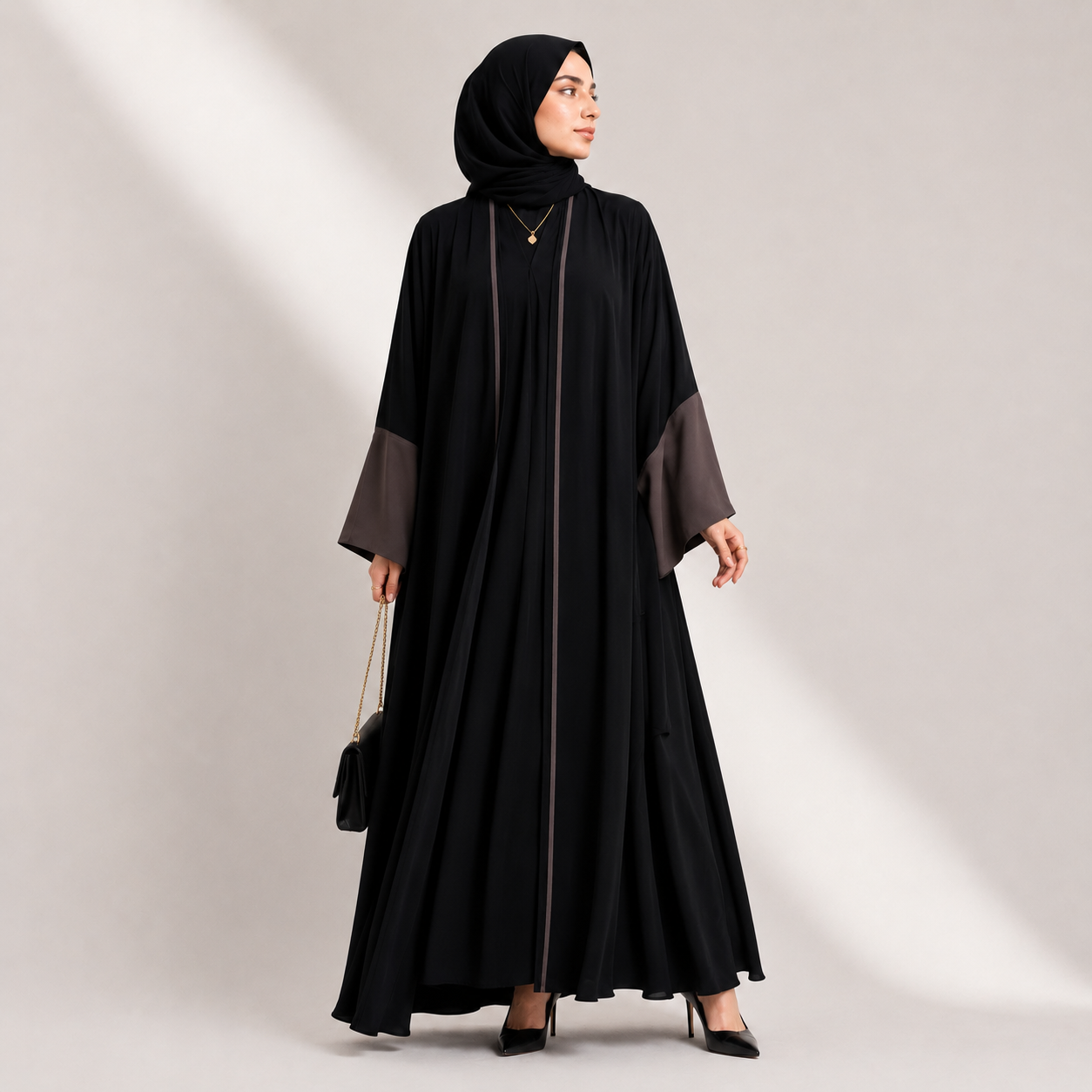 Woman wearing a black abaya with gray sleeves on a light gray background