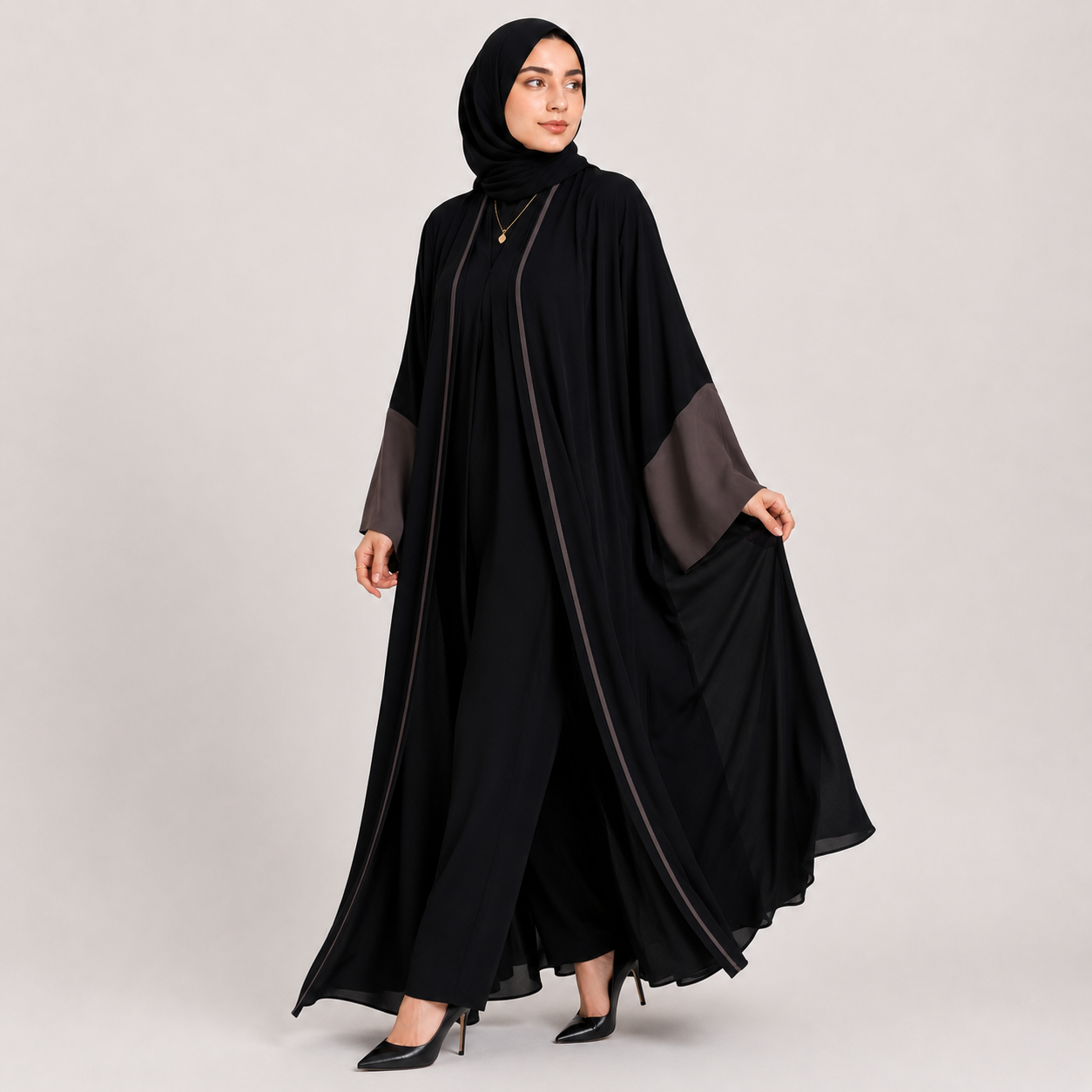 Woman wearing a black abaya with gray accents on a light gray background