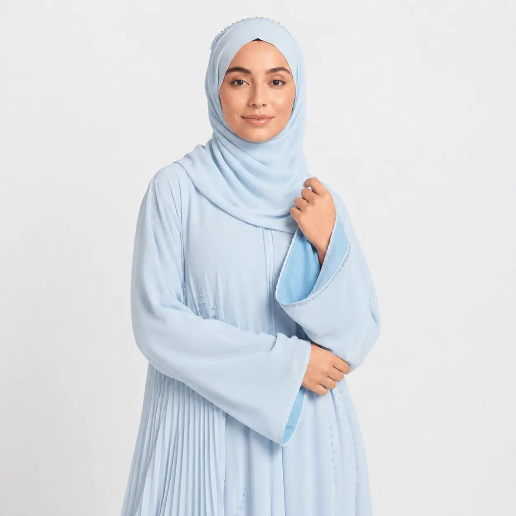 Woman wearing a light blue hijab and dress against a white background