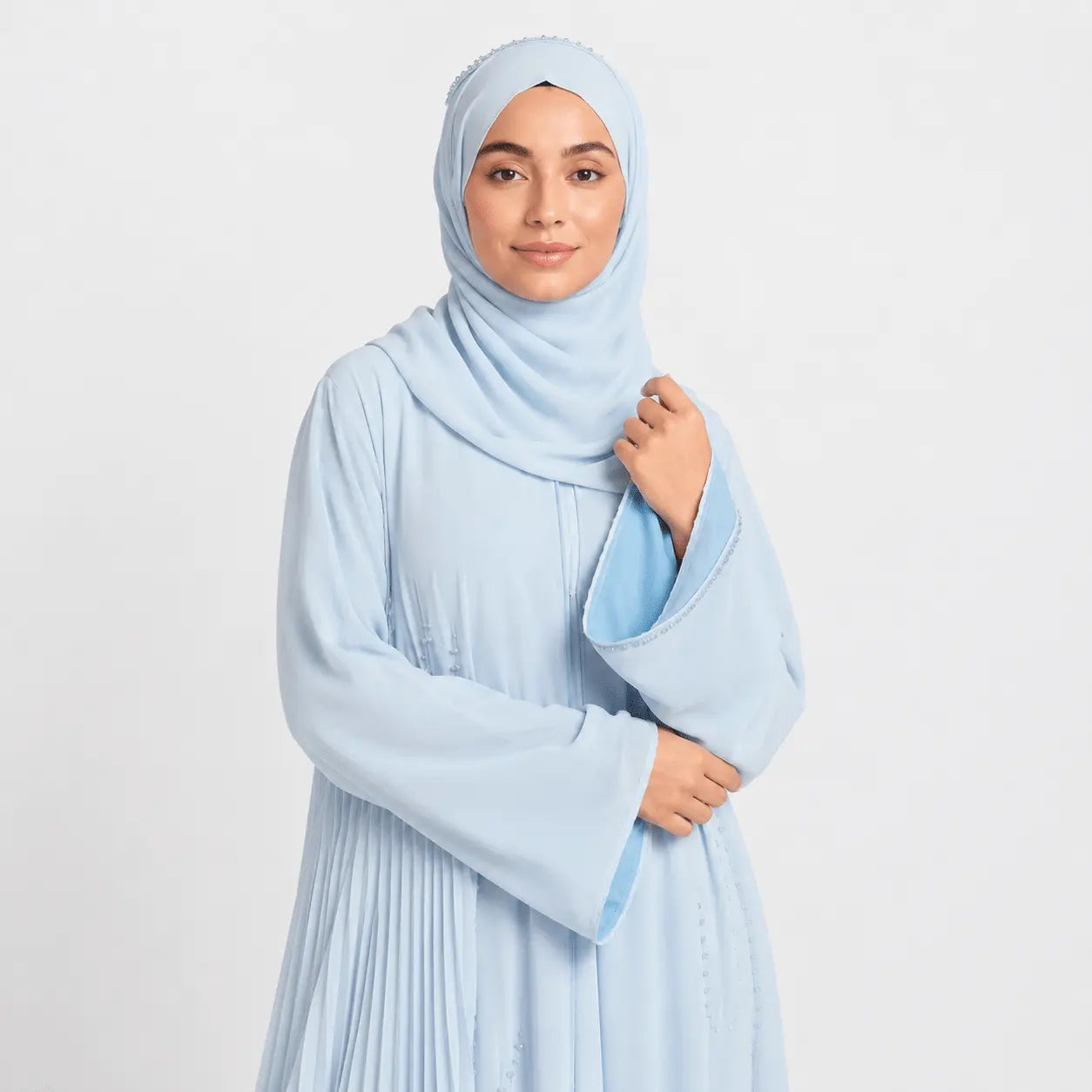 Woman wearing a light blue hijab and dress against a white background