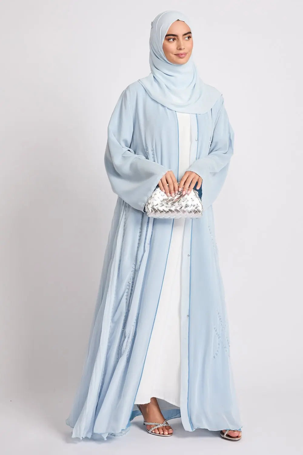 Woman wearing a light blue abaya with a matching hijab on a white background