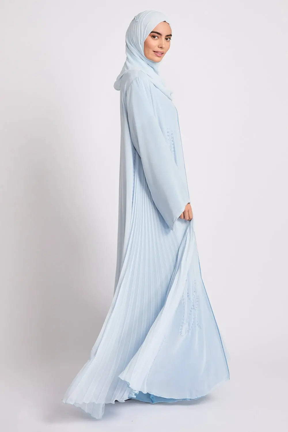 Woman wearing a light blue hijab and dress on a white background