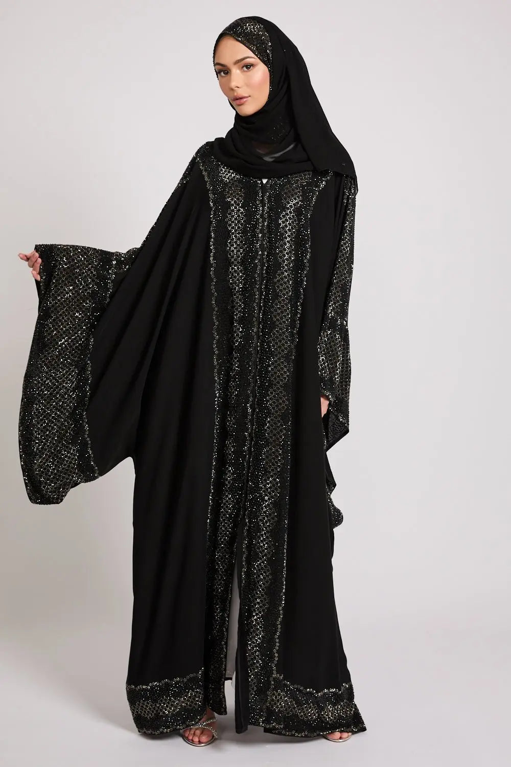 Woman wearing a black abaya with intricate patterns on a white background