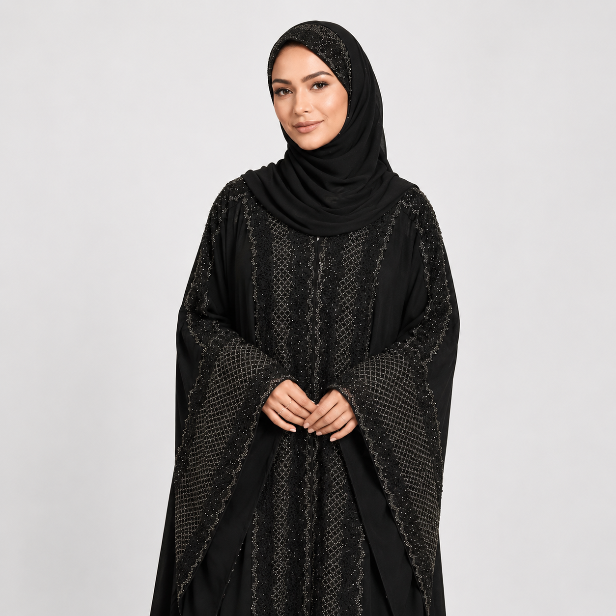 Woman wearing a black hijab and black embroidered dress on a light gray background