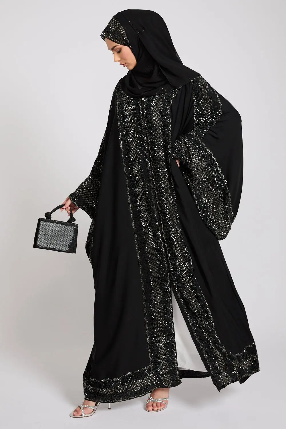 Woman wearing a black abaya with intricate patterns on a white background