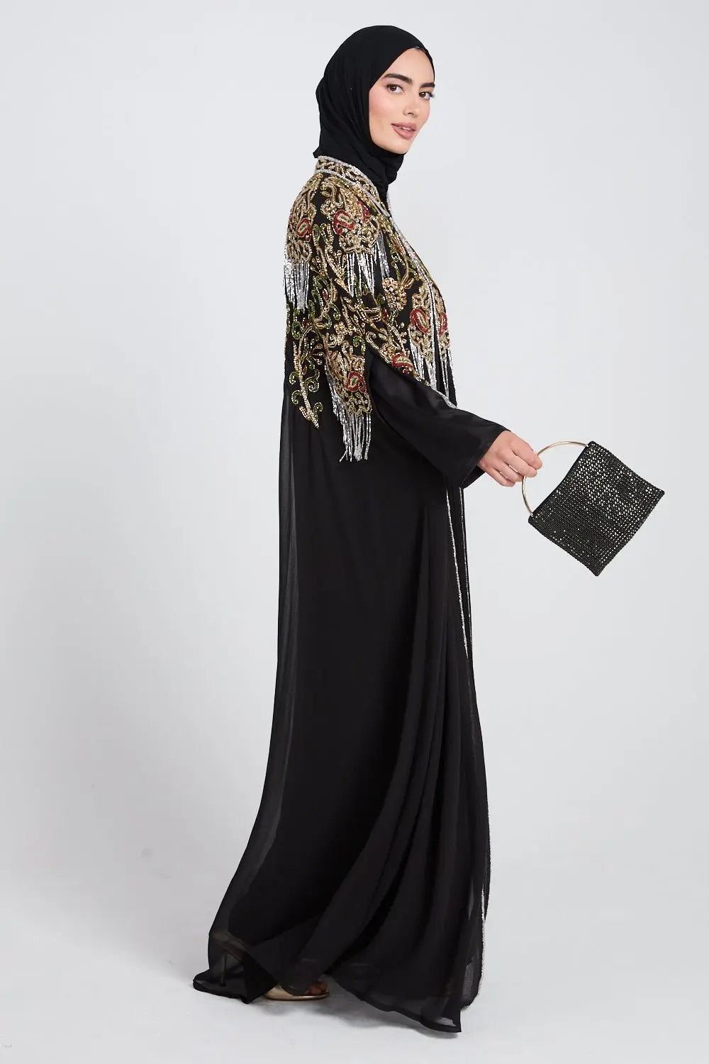 Woman wearing a black abaya with a patterned shawl and holding a matching handbag on a white background