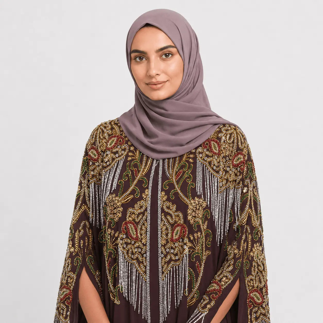 Woman wearing a patterned hijab and shawl on a plain background