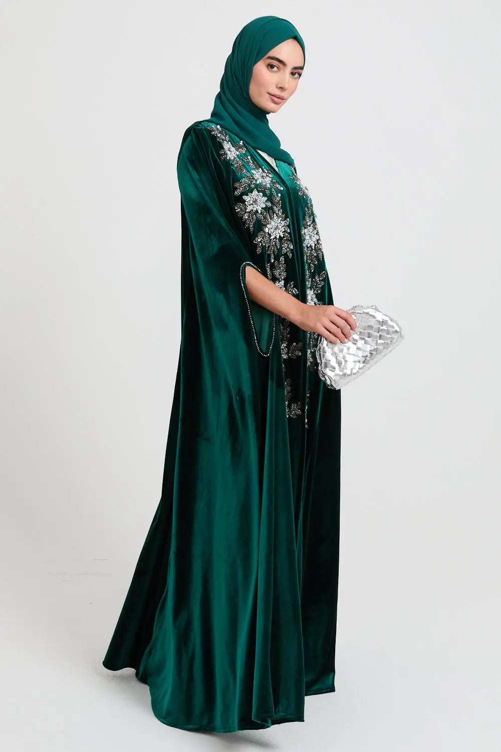 Woman wearing a green abaya with floral embroidery on a white background