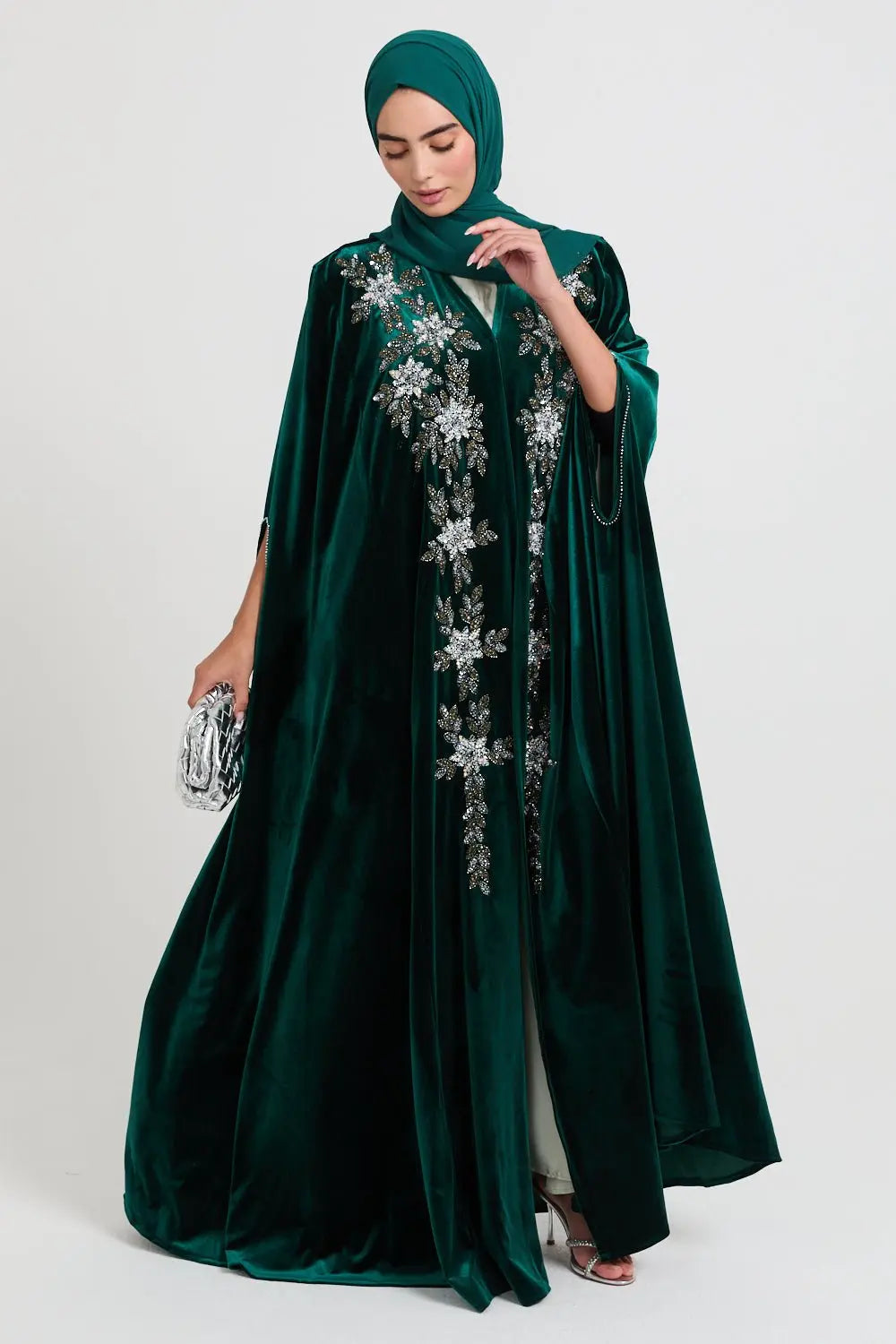 Woman wearing a dark green abaya with floral embroidery on a white background