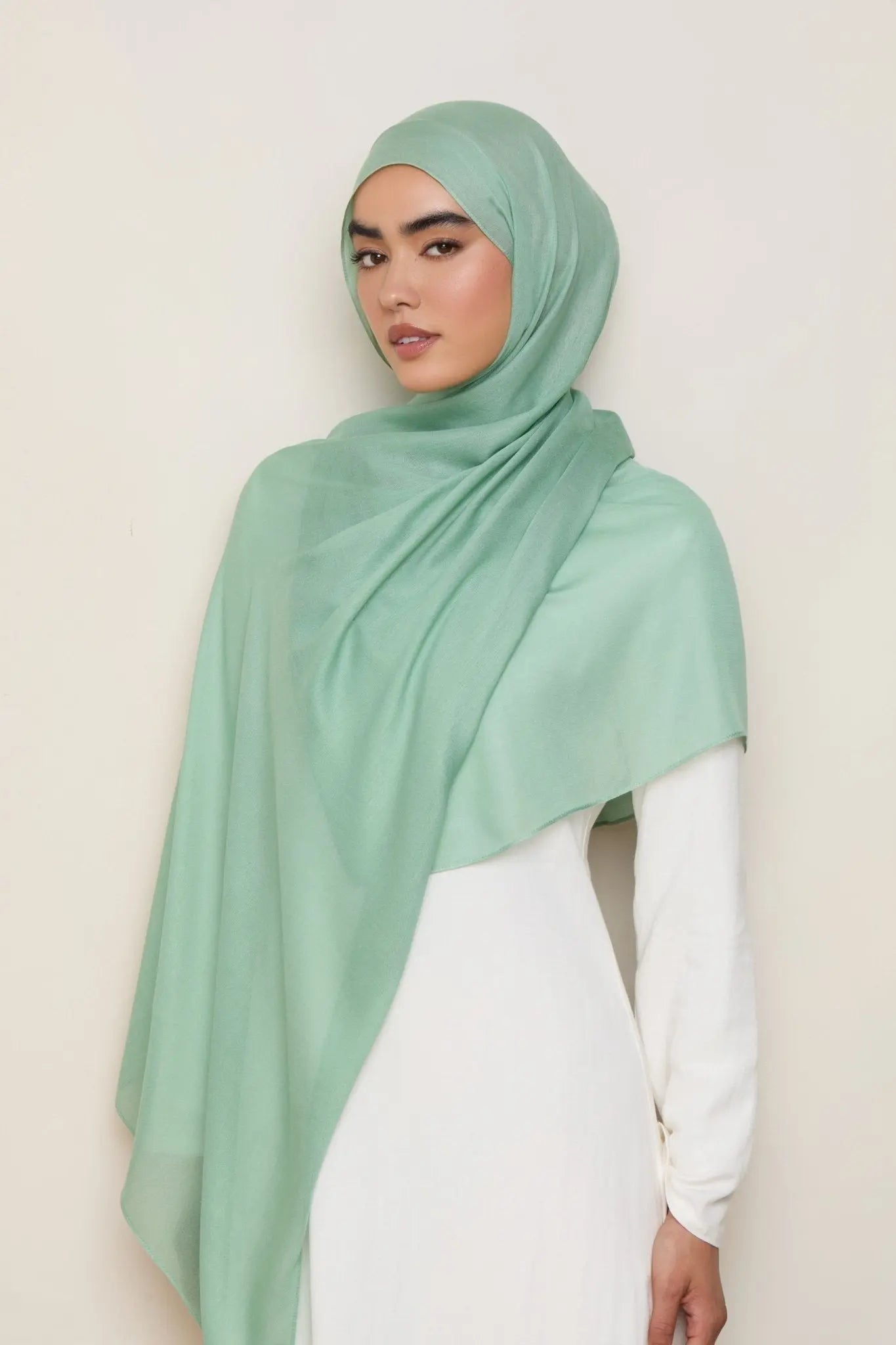 Woman wearing a light green hijab and white top against a plain background