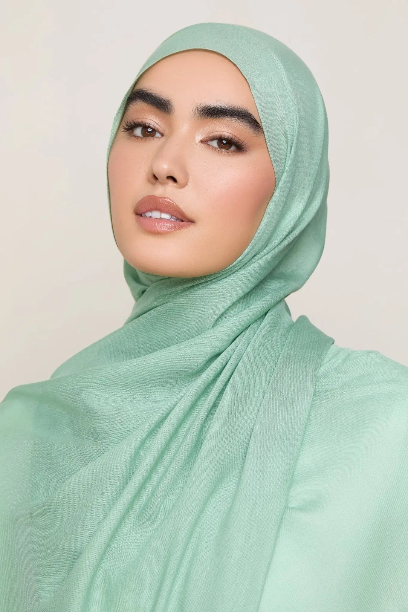 Woman wearing a light green hijab against a plain background