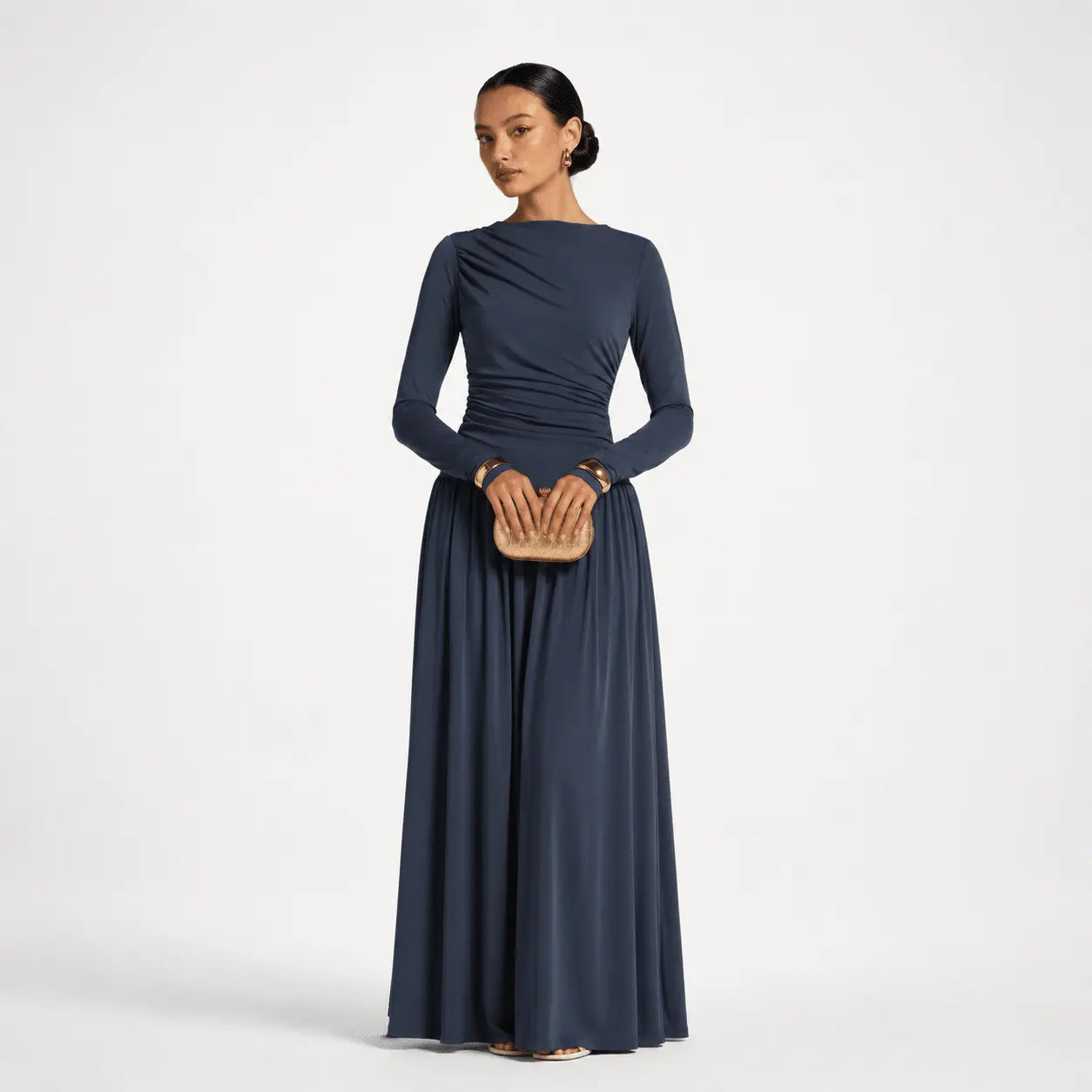 Navy blue long sleeve evening gown with ruched bodice and flowing skirt, styled with gold clutch