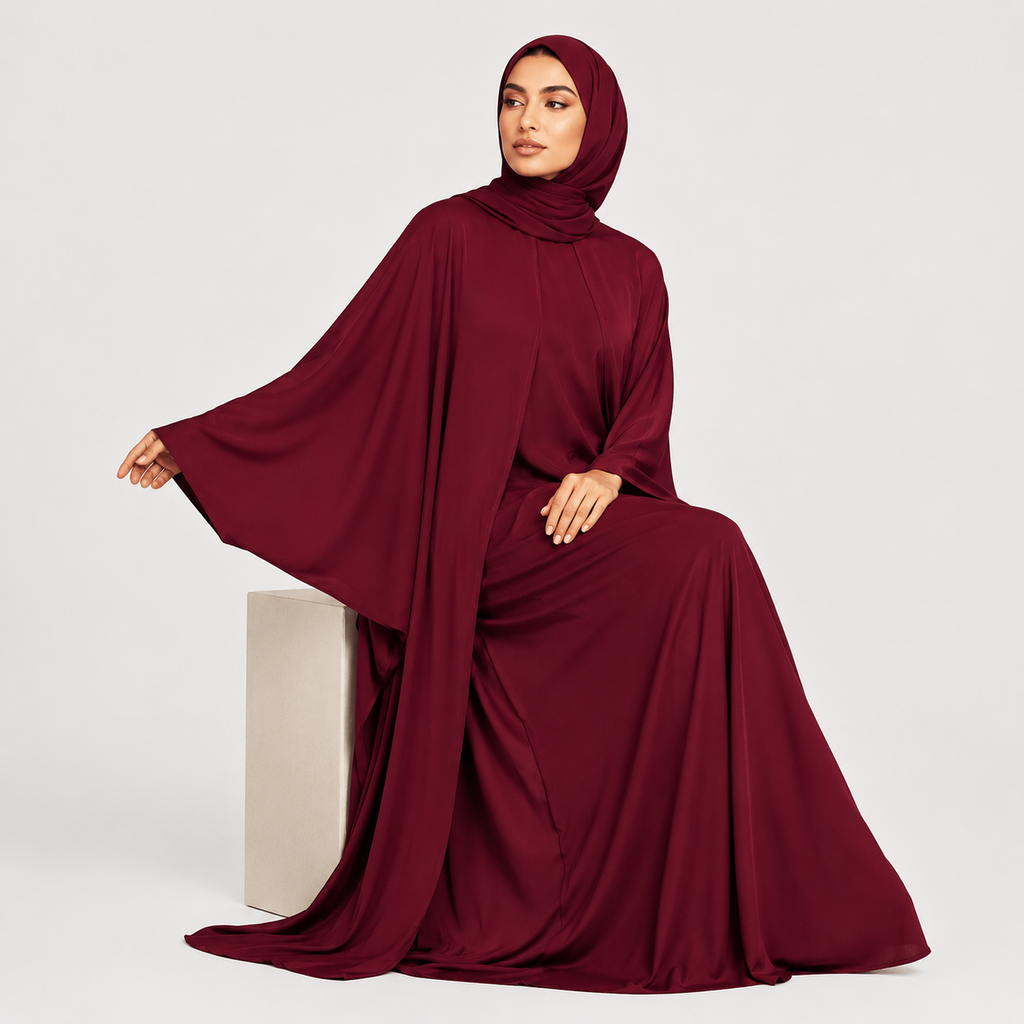 Woman wearing a burgundy abaya sitting on a white cube against a light gray background
