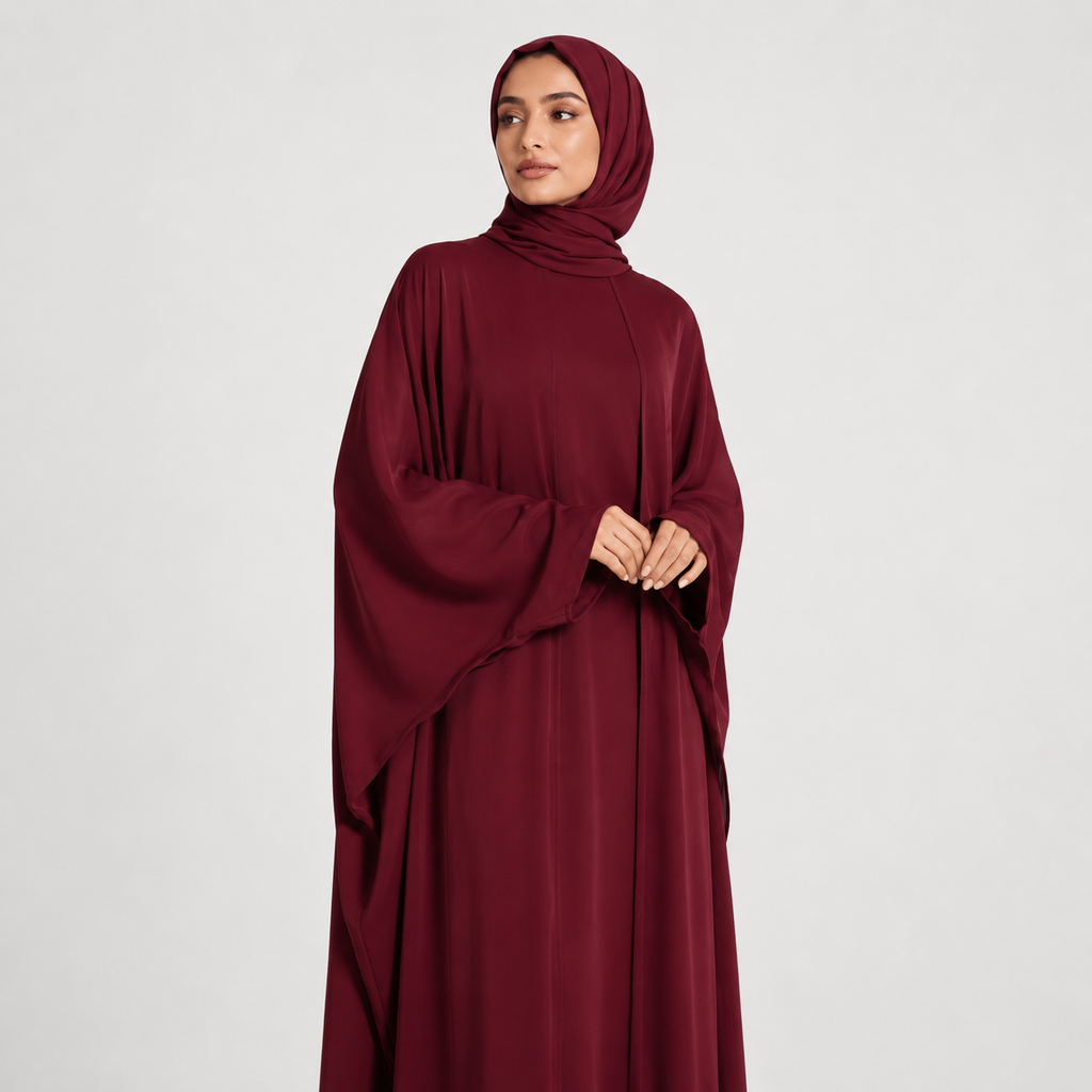 Woman wearing a burgundy abaya and hijab on a white background
