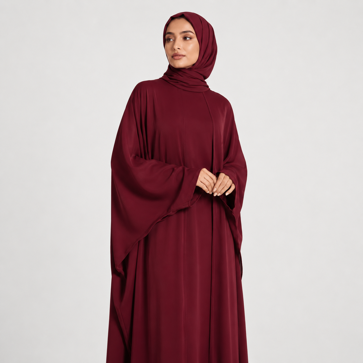 Woman wearing a burgundy abaya and hijab on a white background