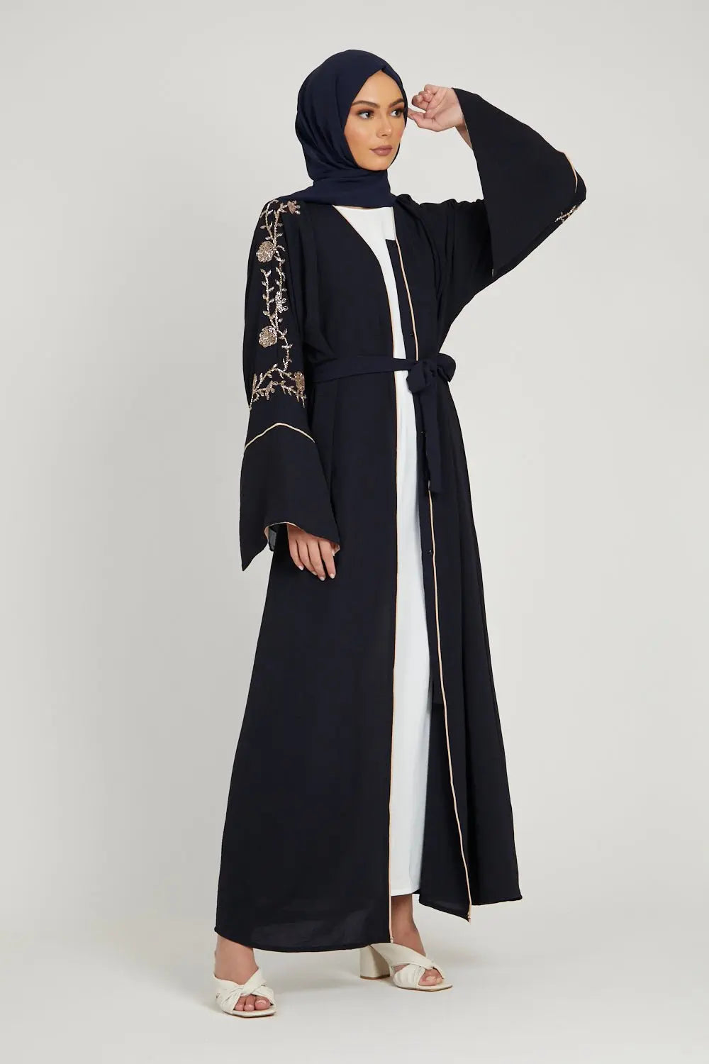 Woman wearing a black abaya with floral embroidery, holding a bouquet of flowers on a white background