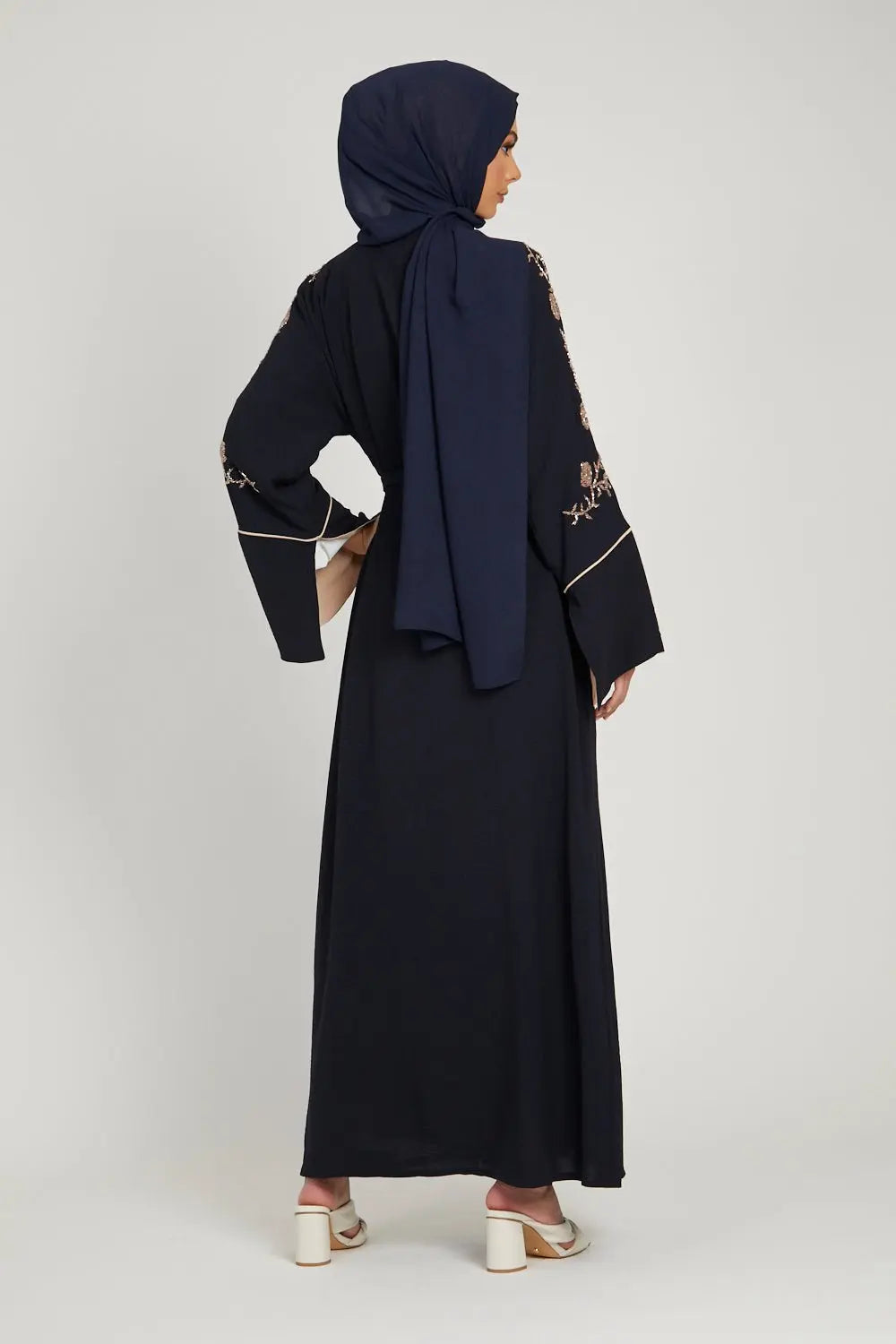 Woman wearing a black abaya with floral embroidery, holding a bouquet of flowers on a white background