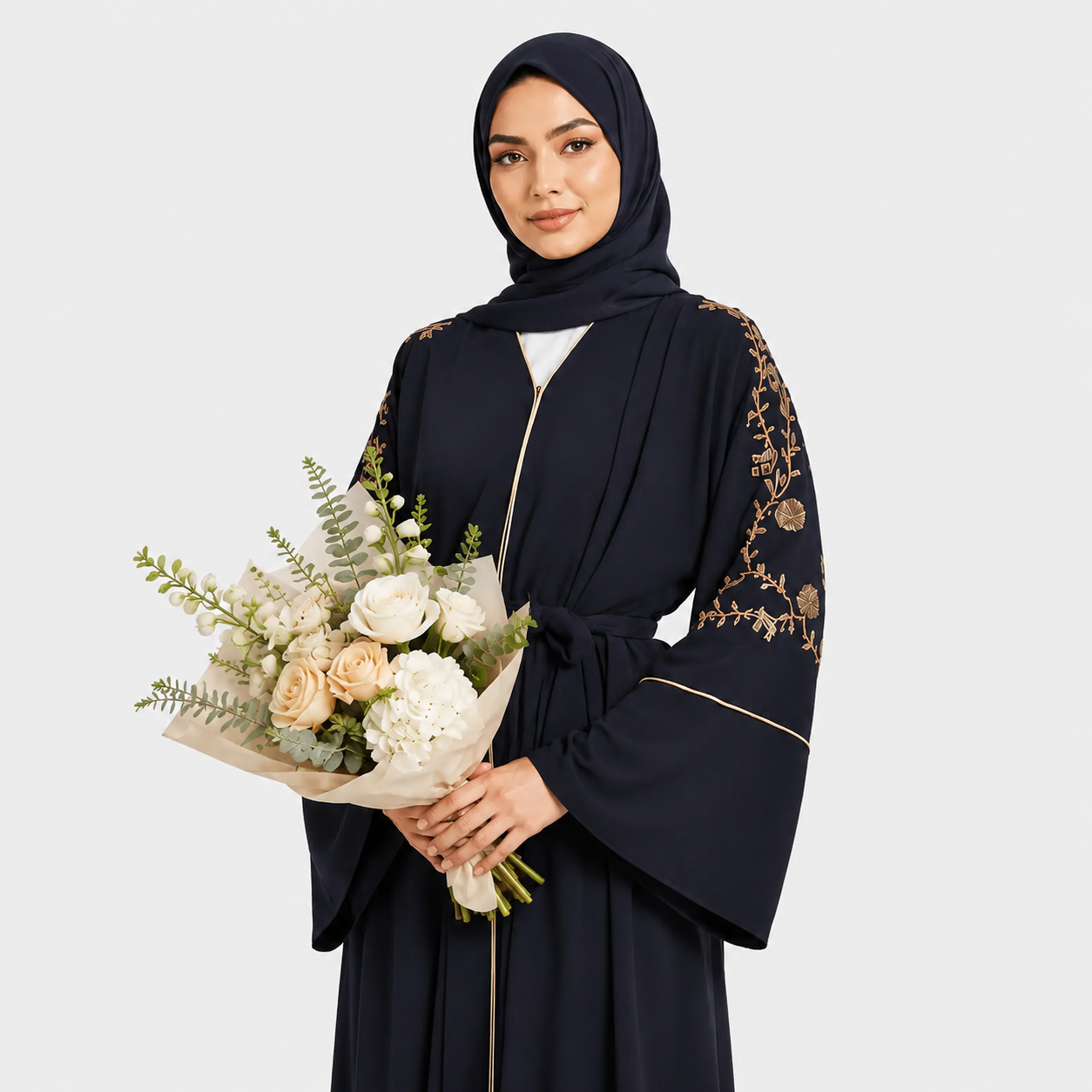Woman in a dark abaya with floral embroidery holding a bouquet of flowers on a light gray background