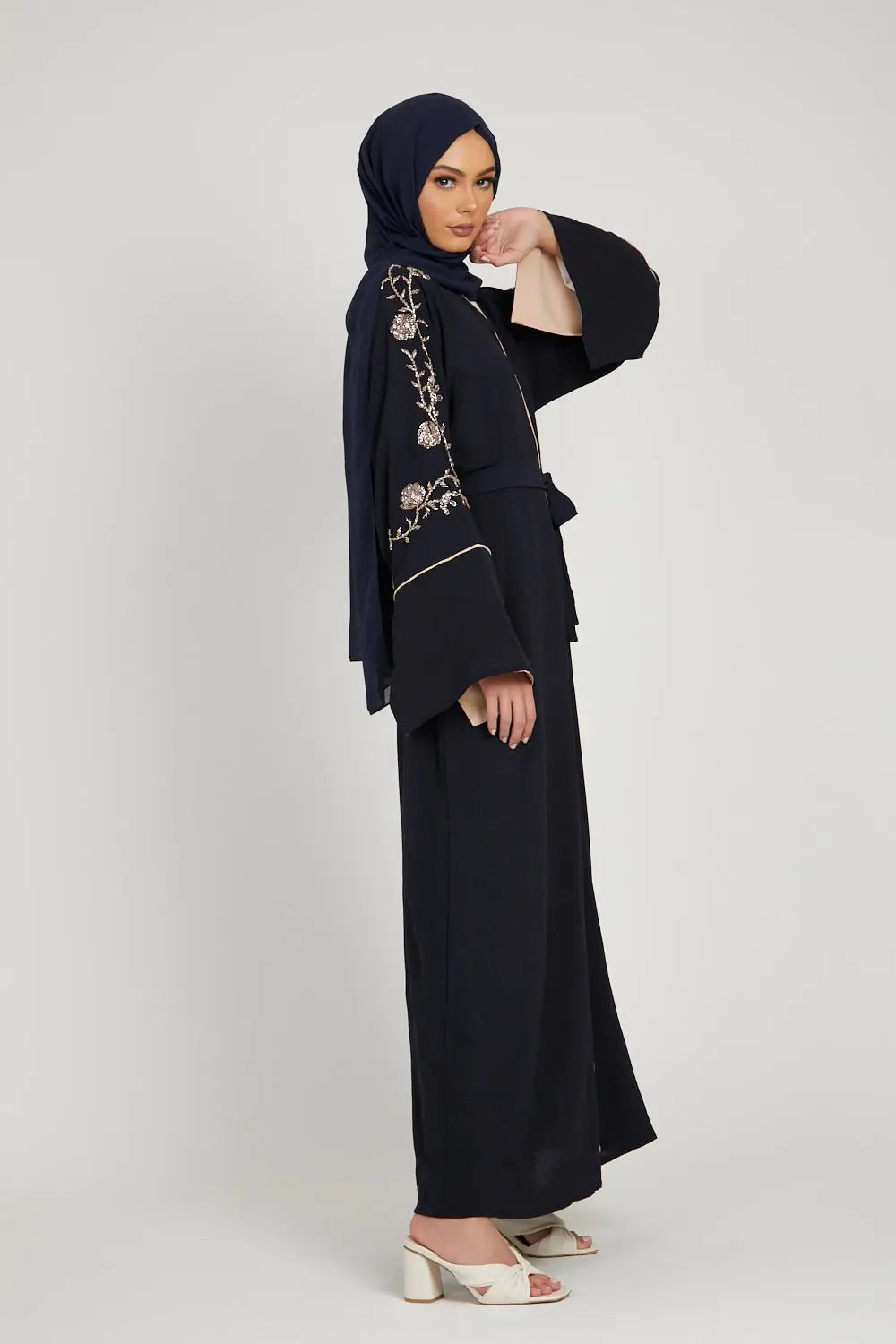 Woman wearing a black abaya with floral embroidery, holding a bouquet of flowers on a white background