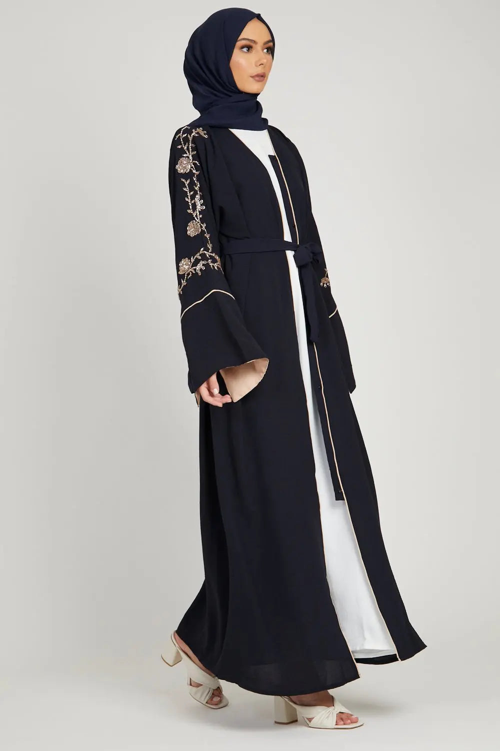 Woman wearing a black abaya with floral embroidery, holding a bouquet of flowers on a white background