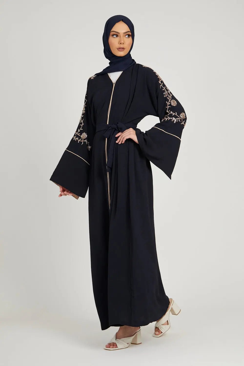 Woman wearing a black abaya with floral embroidery, holding a bouquet of flowers on a white background