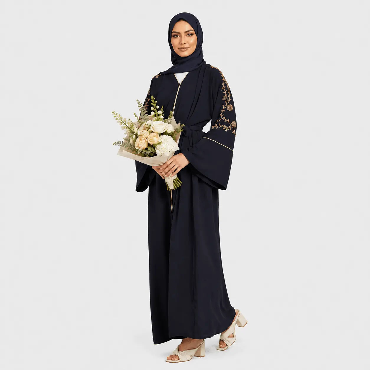 Woman wearing a black abaya with floral embroidery, holding a bouquet of flowers on a white background