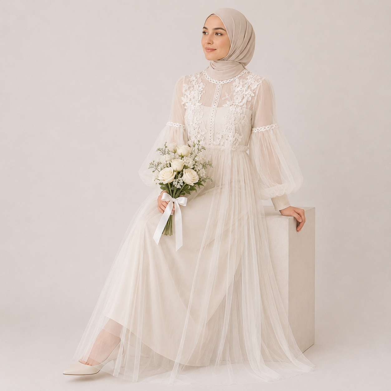 Woman in a white lace dress holding flowers against a plain background