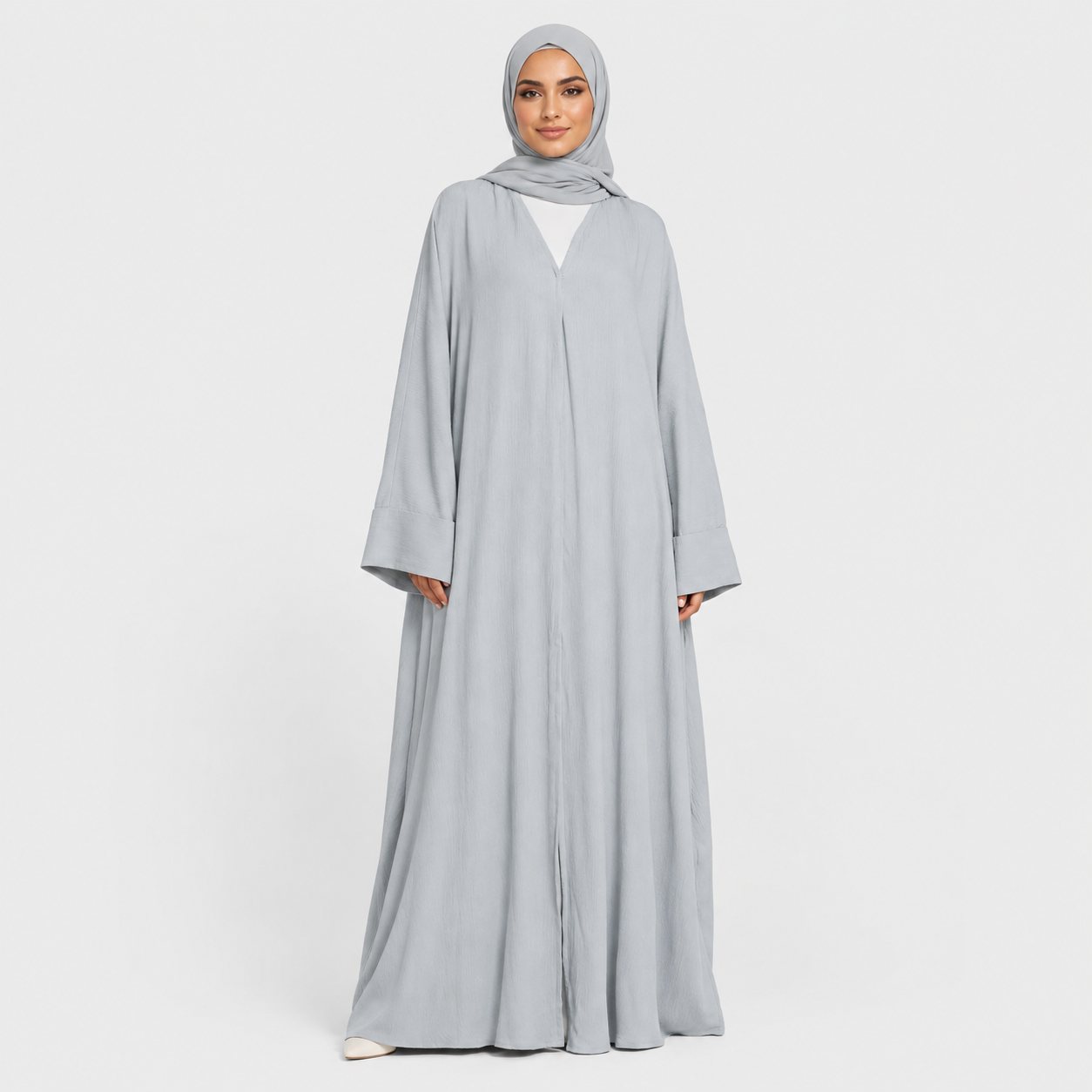 Woman wearing a light gray abaya and hijab on a white background