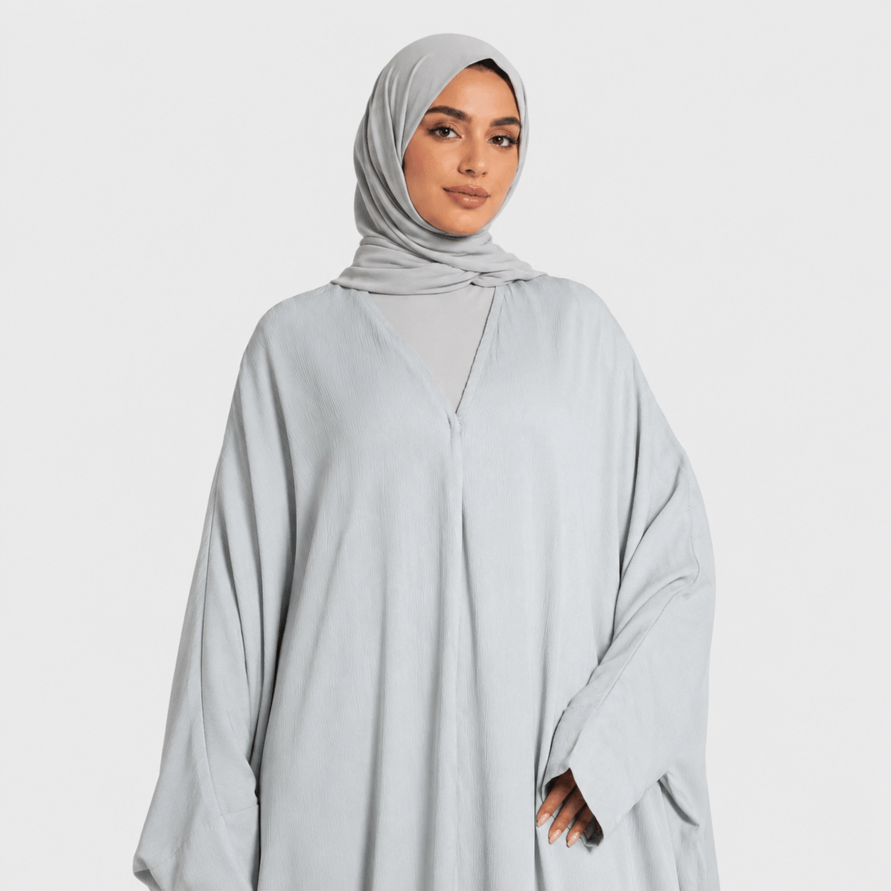 Woman wearing a light gray hijab and matching outfit on a white background