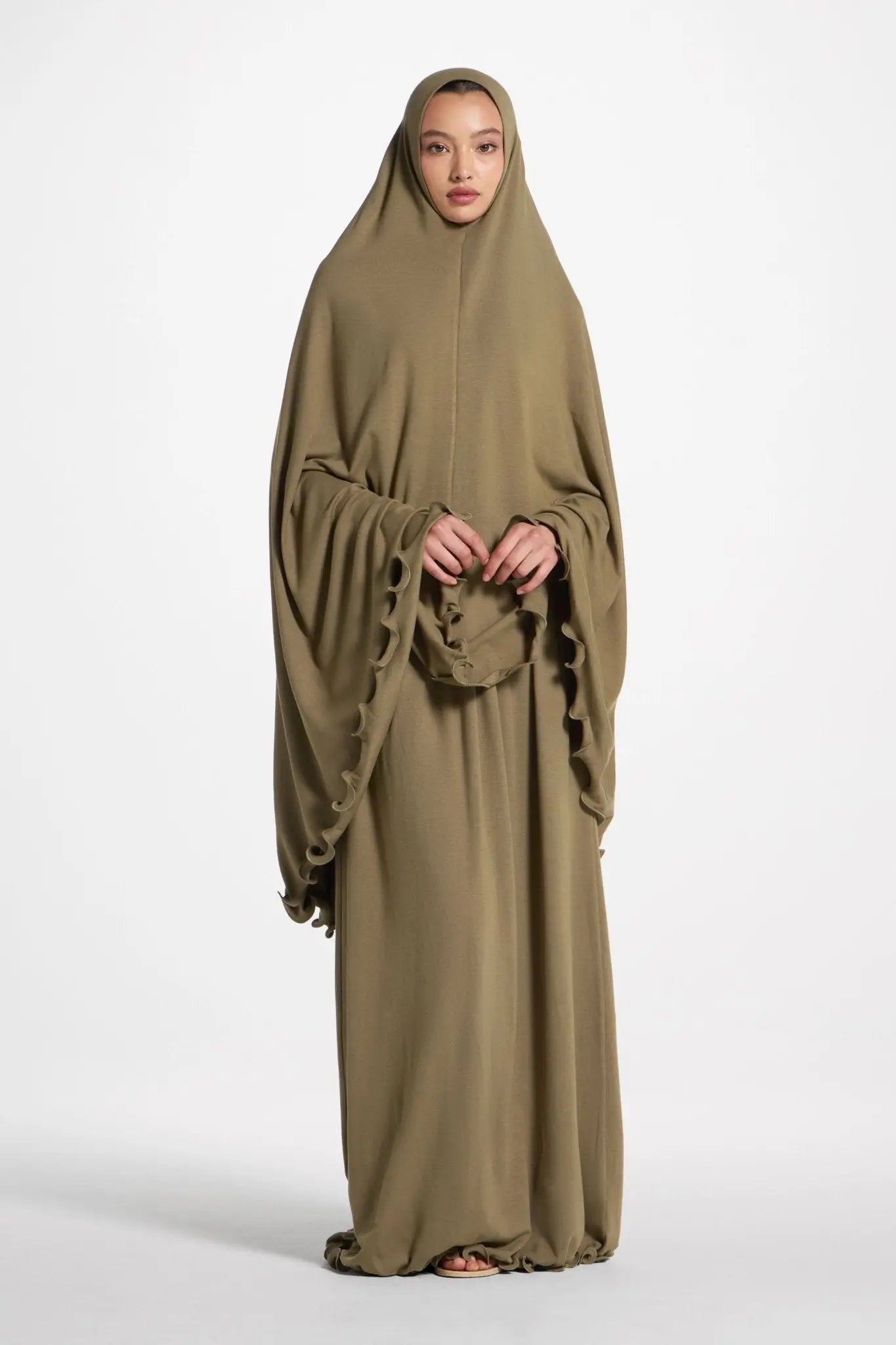Woman wearing a long, flowing olive green abaya on a white background