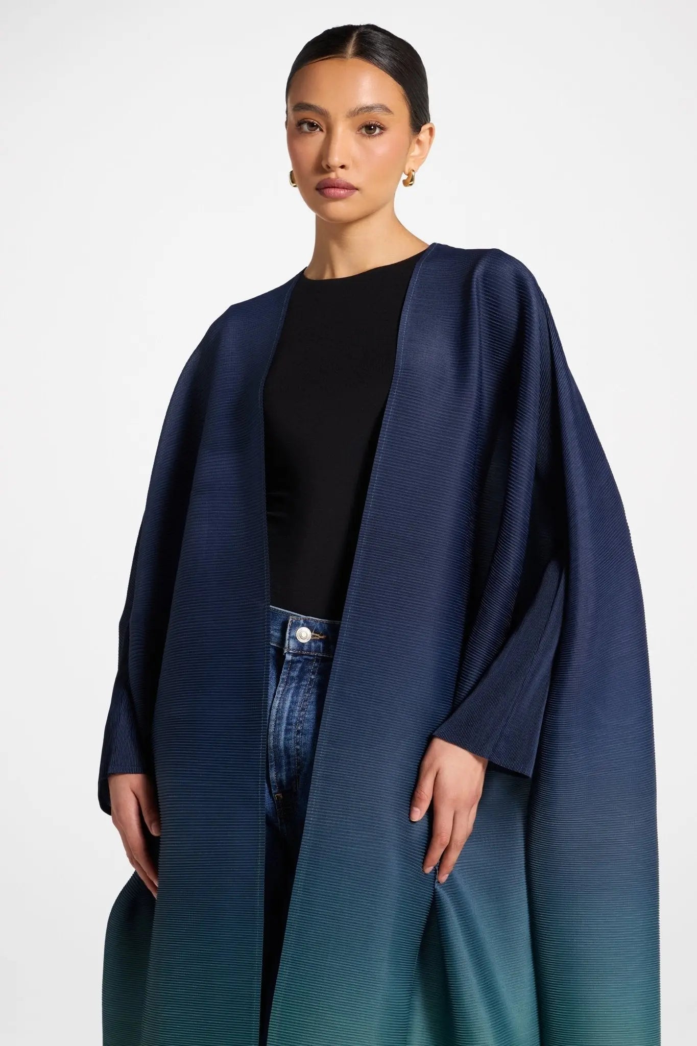 Woman wearing a navy blue coat over a black top and jeans on a white background