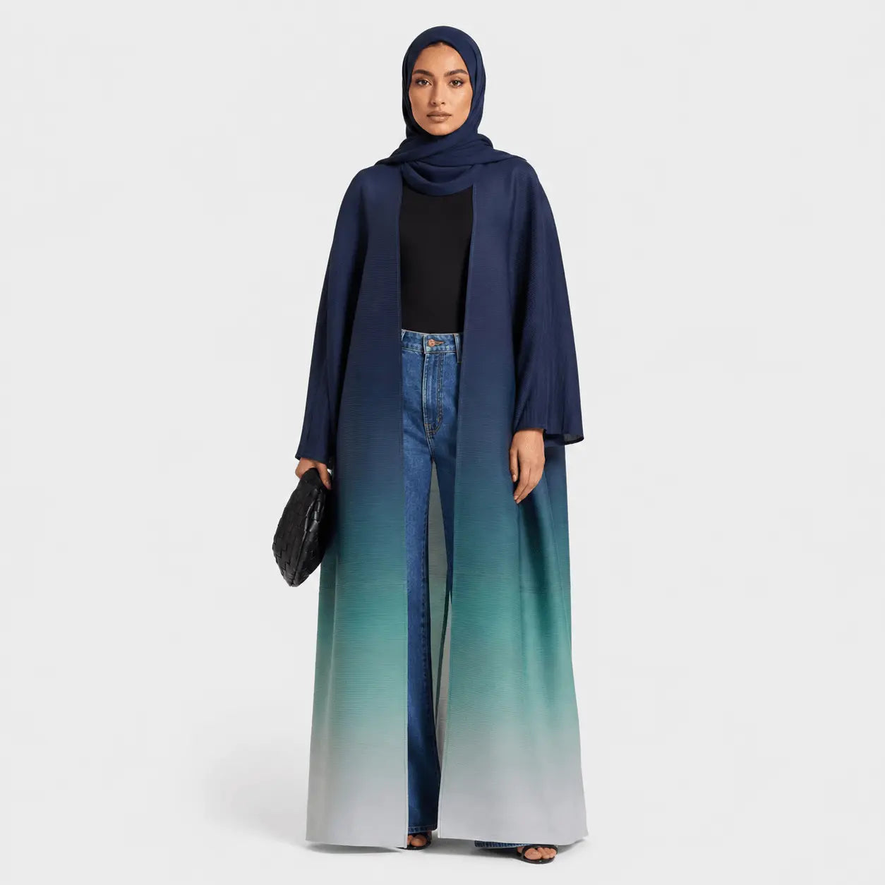 Woman wearing a long, gradient blue coat with wide-leg jeans on a white background