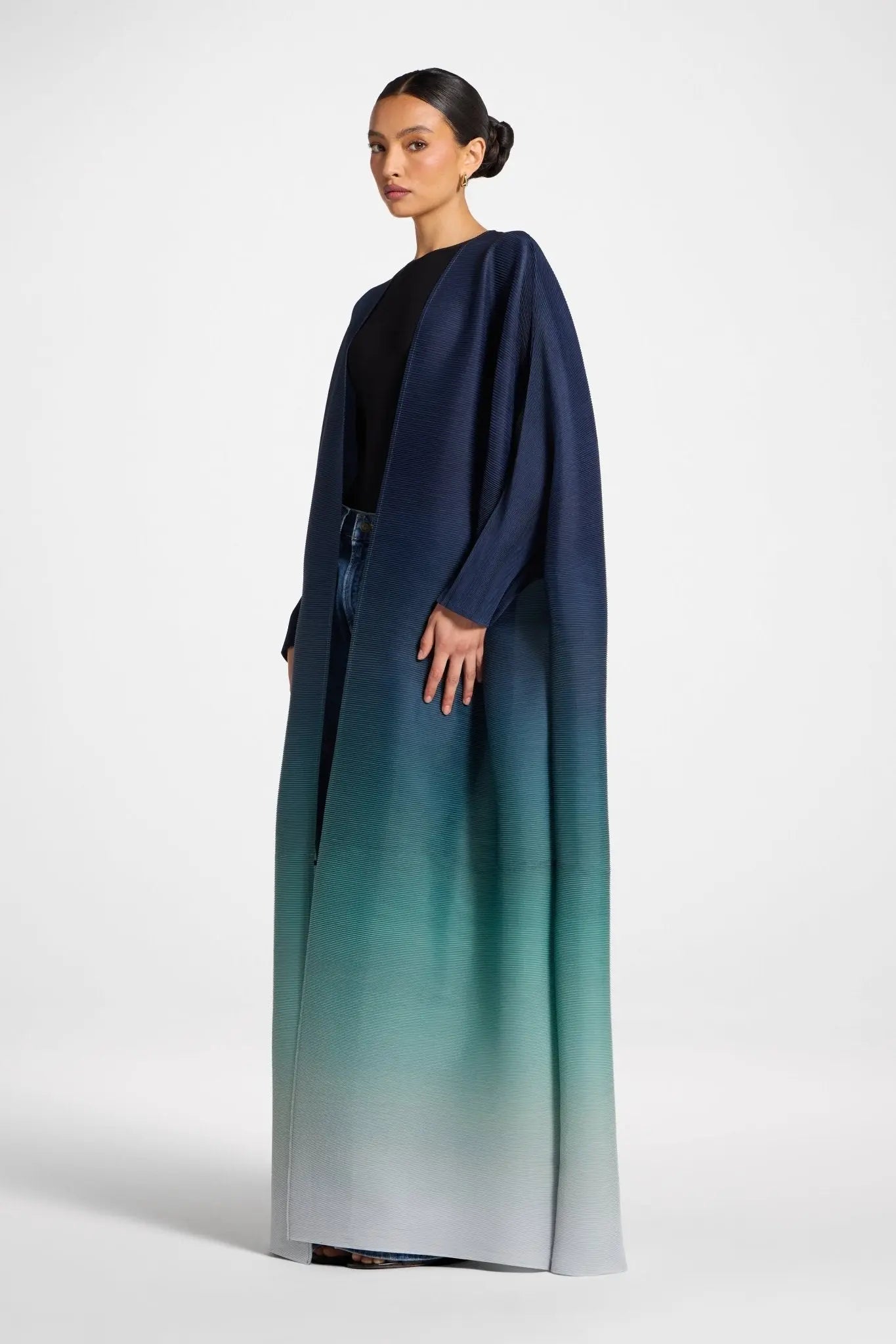 Woman wearing a long, gradient dress with a black top and blue-green skirt on a white background