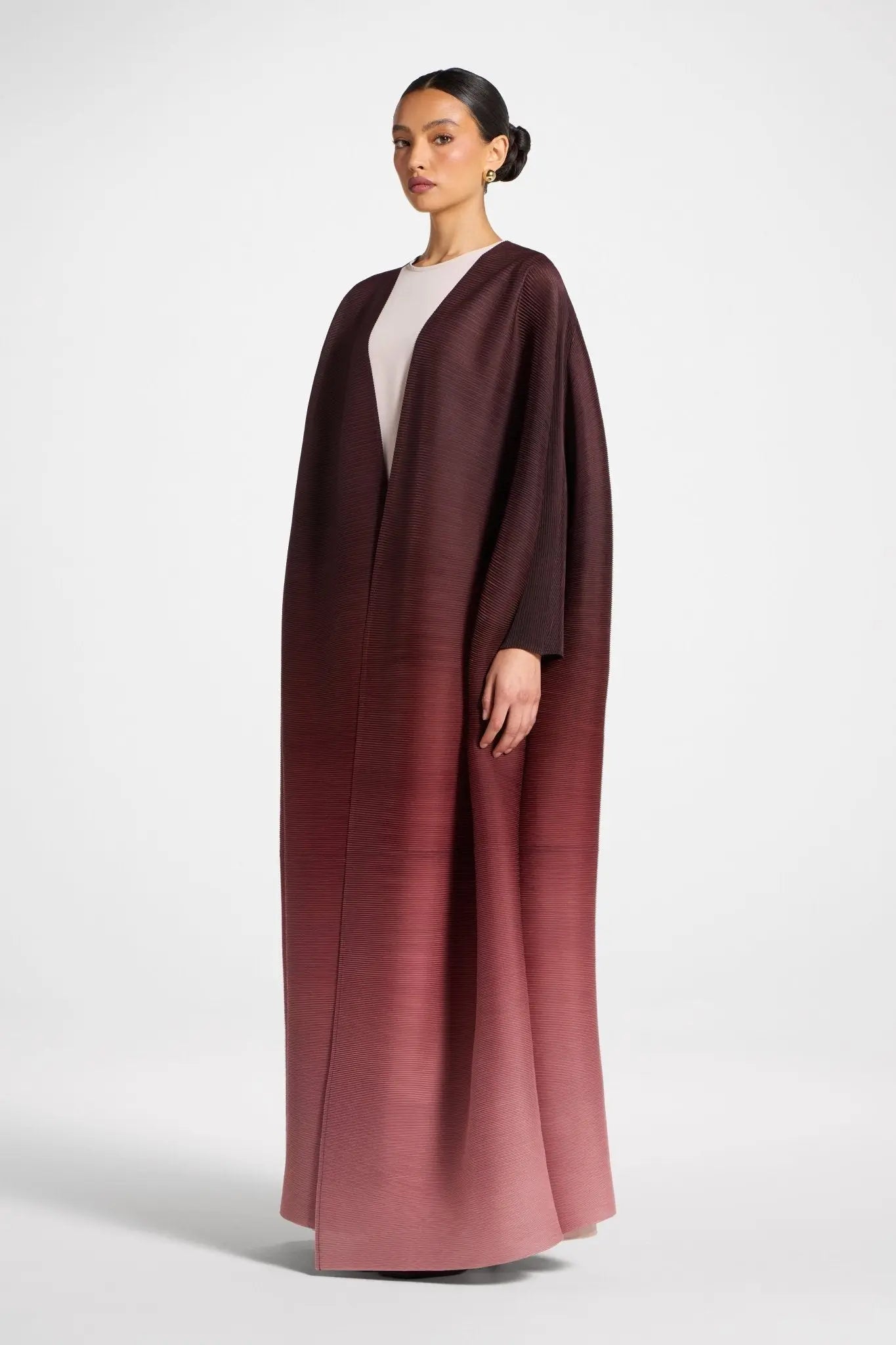 Woman wearing a long, dark brown robe over a white top on a light gray background
