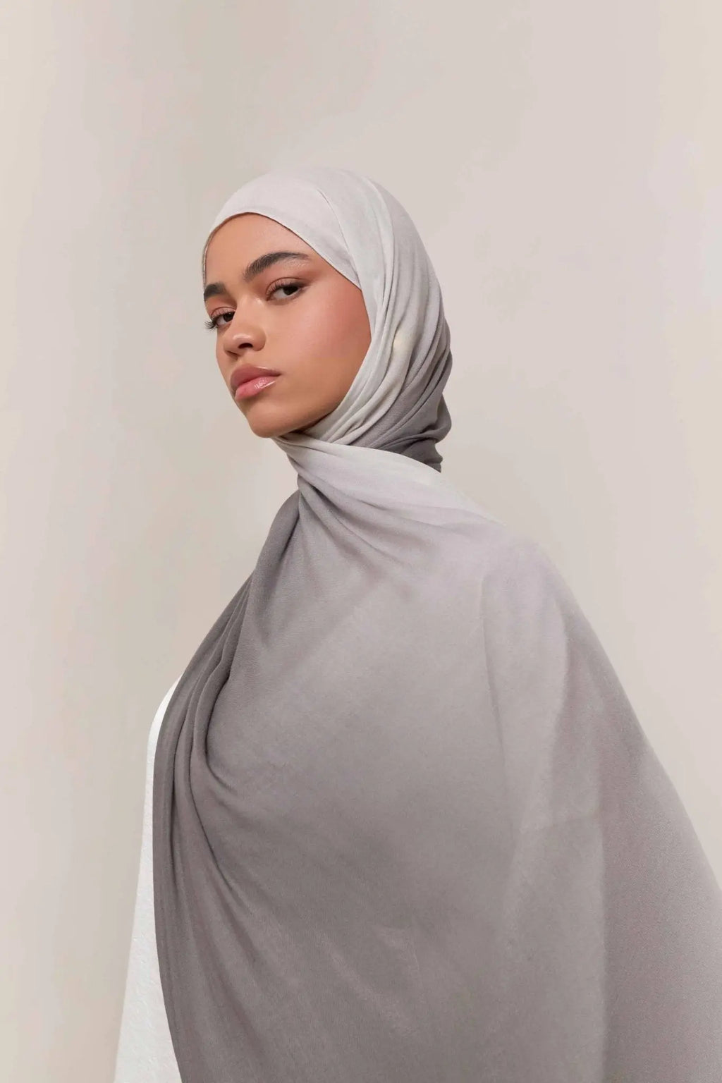 Woman wearing a light gray hijab against a plain background
