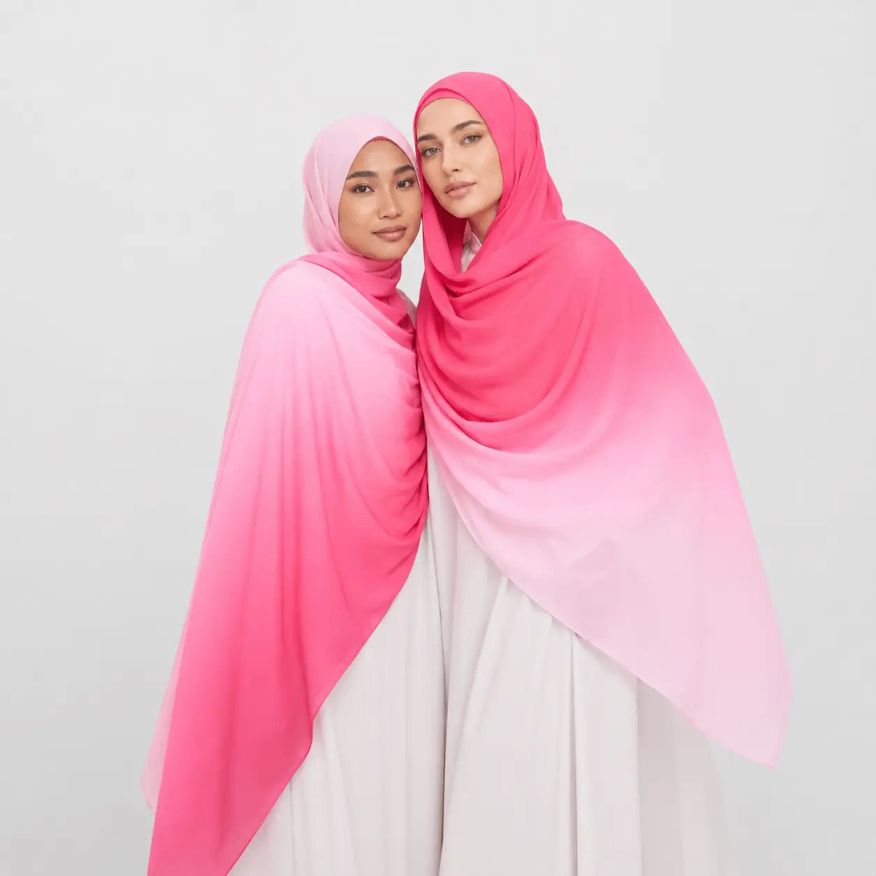 Two women wearing pink and white gradient hijabs on a light gray background
