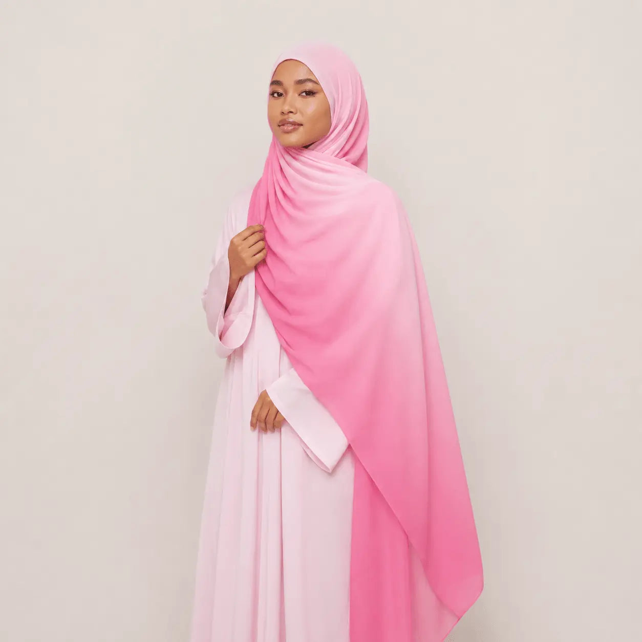 Woman wearing a pink hijab and dress against a plain background