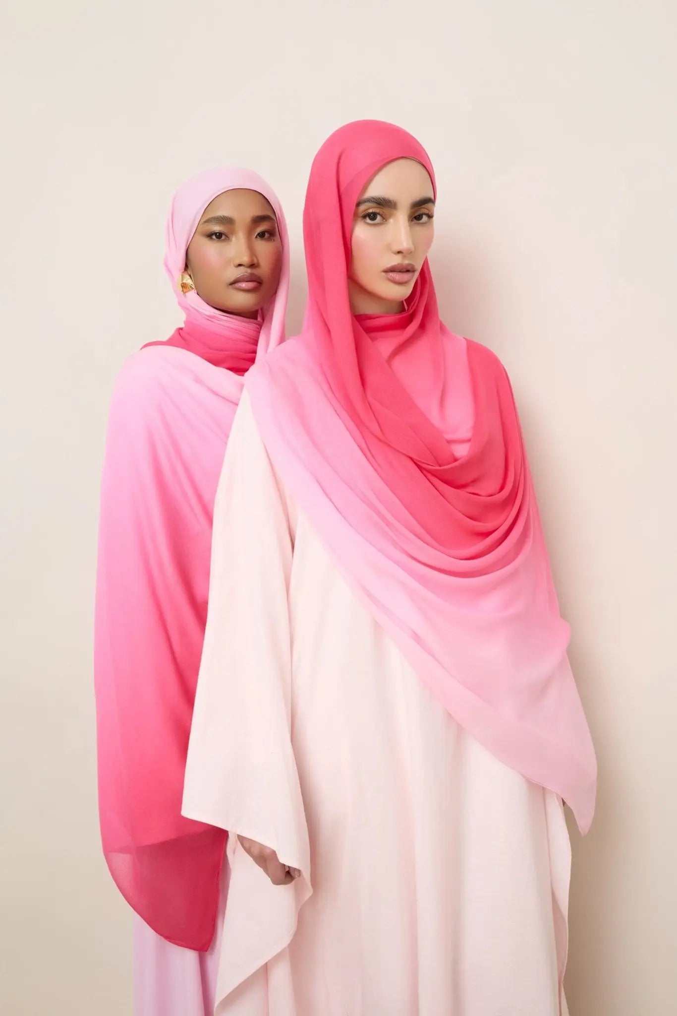 Two women wearing pink and white gradient hijabs against a plain background