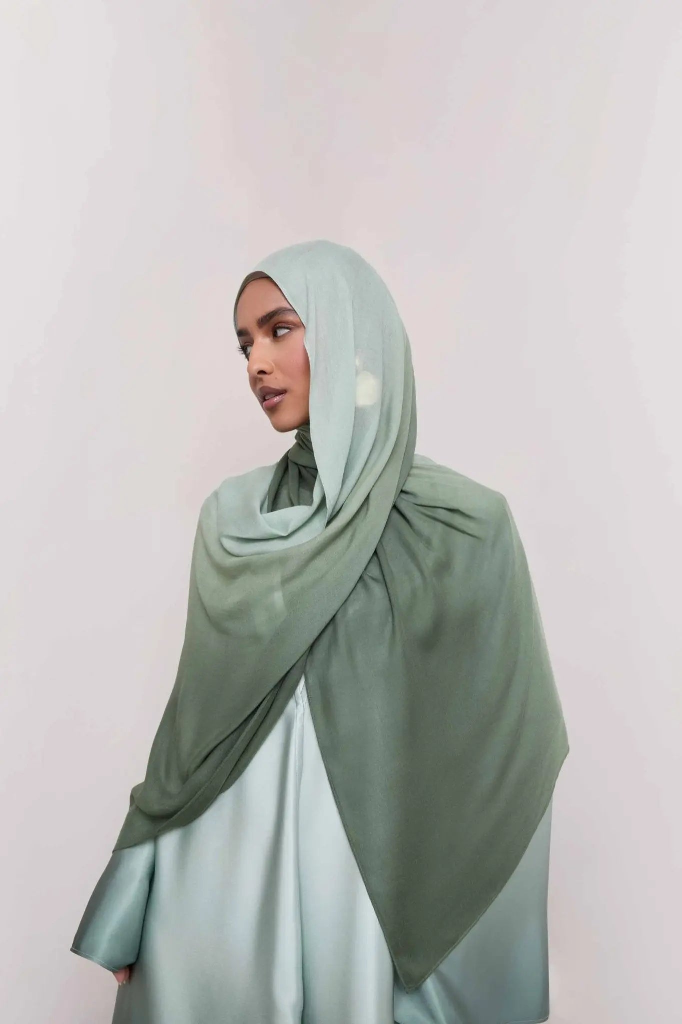 Person wearing a light green hijab and dress against a white background