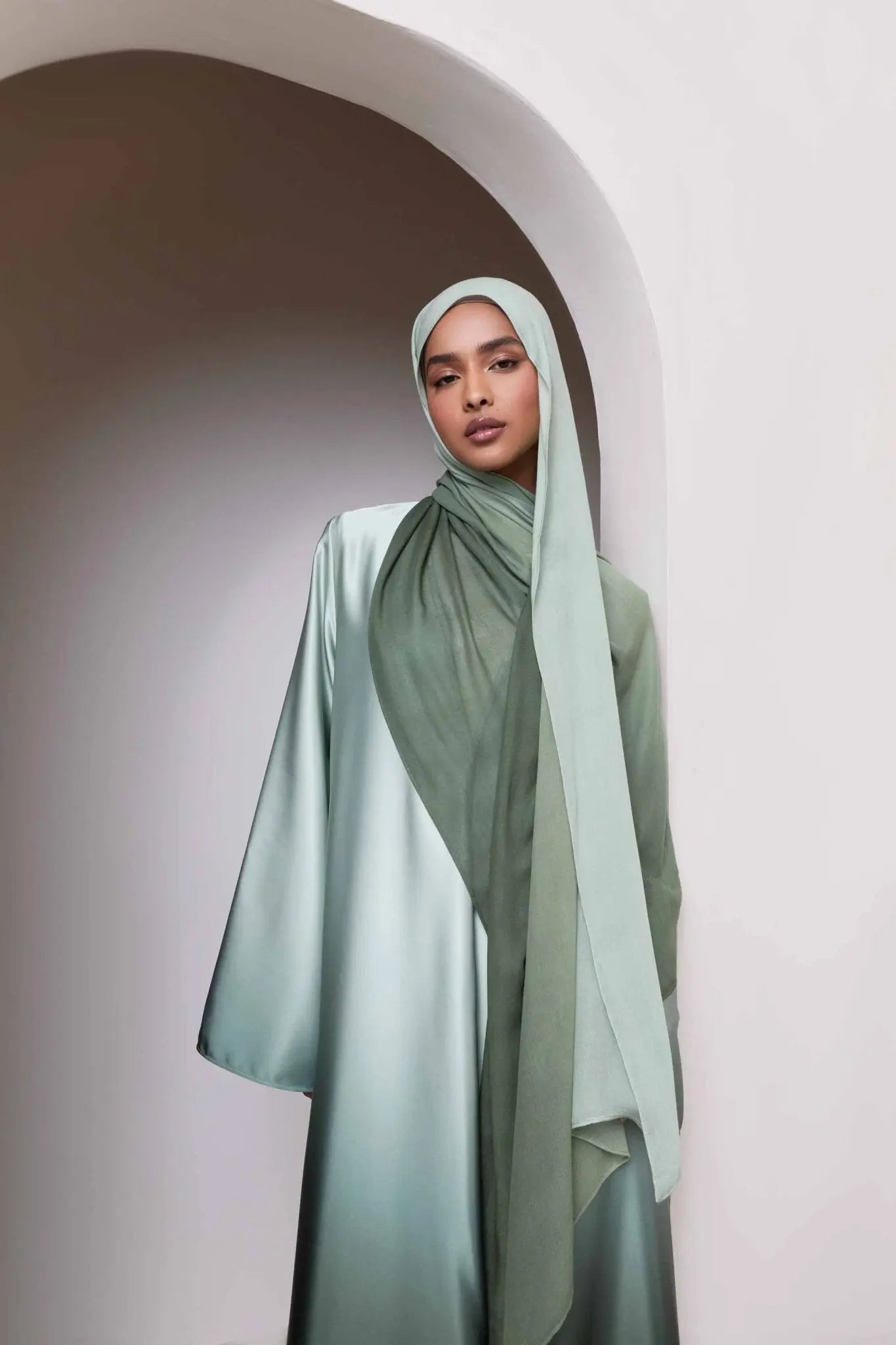 Woman wearing a light green hijab and dress standing against a neutral background
