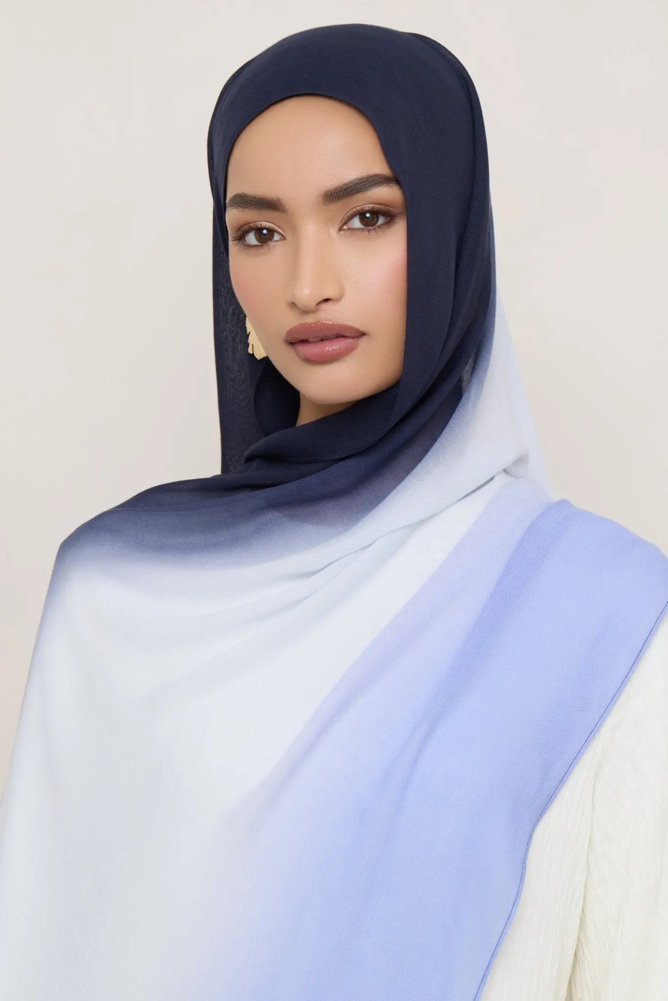 Woman wearing a navy hijab with a light blue scarf on a plain background