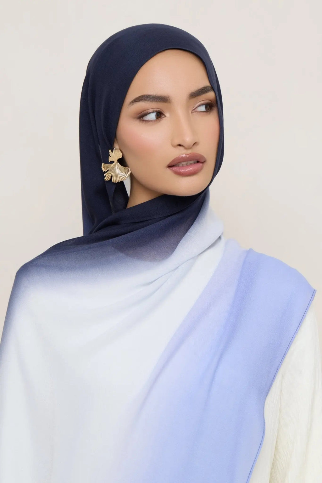 Woman wearing a navy hijab with a light blue scarf on a plain background